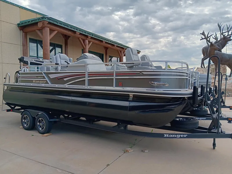 Slide: The Image of 2023 Ranger 223F pontoon boat on a trailer outside a building with statues. - 0