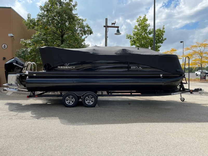 Slide: The Image of 2023 Regency 230 LE3 pontoon boat on a trailer, covered and parked outdoors. - 15