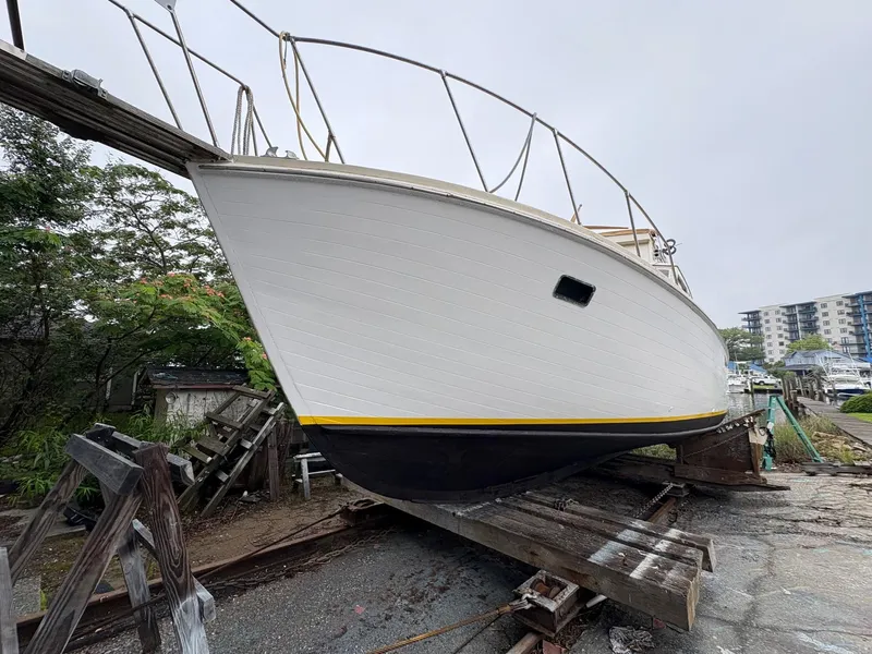 Slide: The Image of 1963 Egg Harbor Convertible Cruiser on dry dock, white hull with yellow stripe, overcast sky. - 3