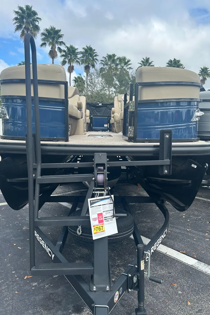 Slide: The Image of 2023 Regency 250 LE3 pontoon boat on trailer, palm trees in background. - 0