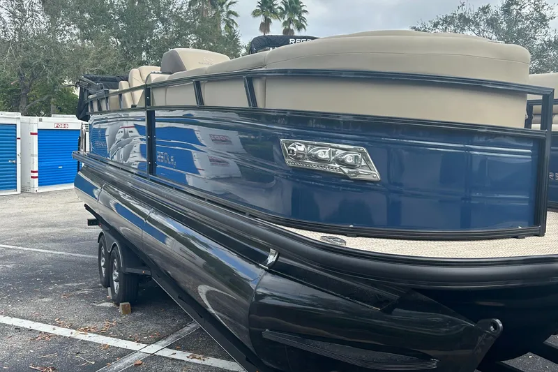 Slide: The Image of 2023 Regency 250 LE3 pontoon boat with blue and beige exterior in a parking lot. - 1