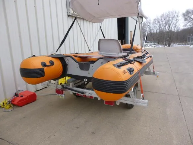 Slide: The Image of 2015 Sea Eagle 14' inflatable boat on trailer, orange and black, parked outside. - 2