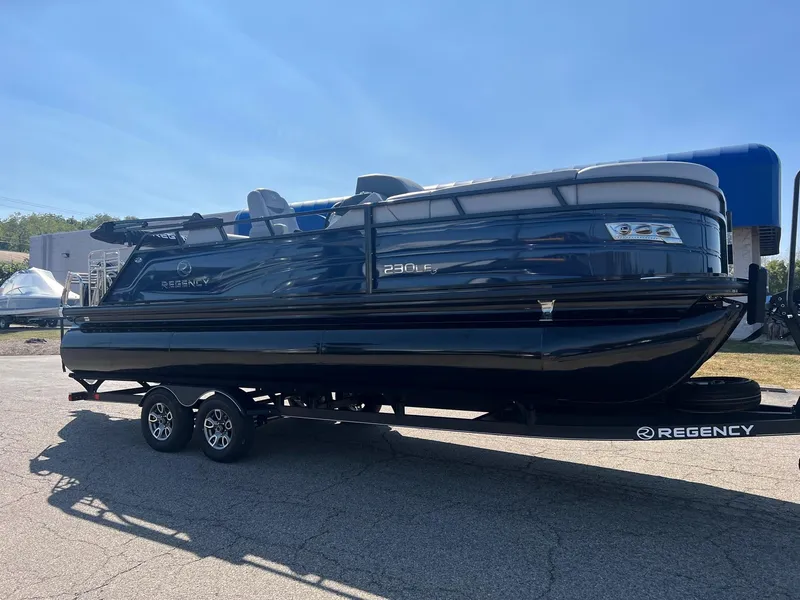Slide: The Image of 2023 Regency 230 LE3 Sport pontoon boat on trailer, parked outdoors. - 0