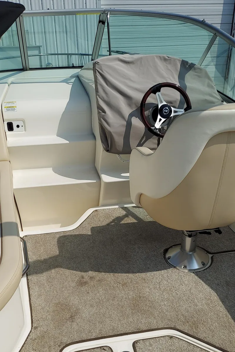 Slide: The Image of 2012 Sea Ray 240 Sundancer boat helm with covered steering wheel and beige seating. - 9
