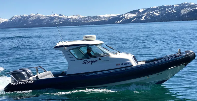 Slide: The Image of 2003 Protector Targa 28 boat cruising on a lake with snowy mountains in the background. - 0