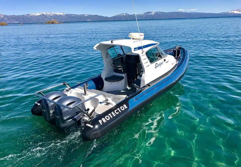 Slide: The Image of 2003 Protector Targa 28 boat on clear blue water with scenic mountain backdrop. - 2