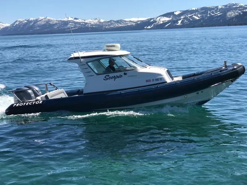 Slide: The Image of 2003 Protector Targa 28 boat cruising on a clear blue lake with snowy mountains. - 5