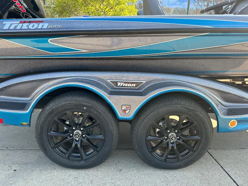 Slide: The Image of 2023 Triton 19 TrX boat trailer with dual black wheels and blue accents. - 3