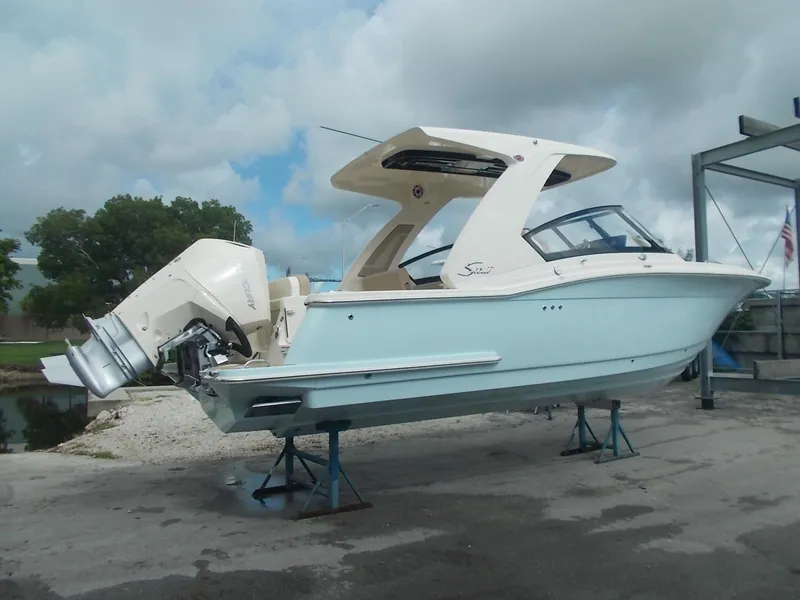 Slide: The Image of 2025 Scout 277 Dorado boat on stands, light blue hull, outboard motor, cloudy sky. - 2