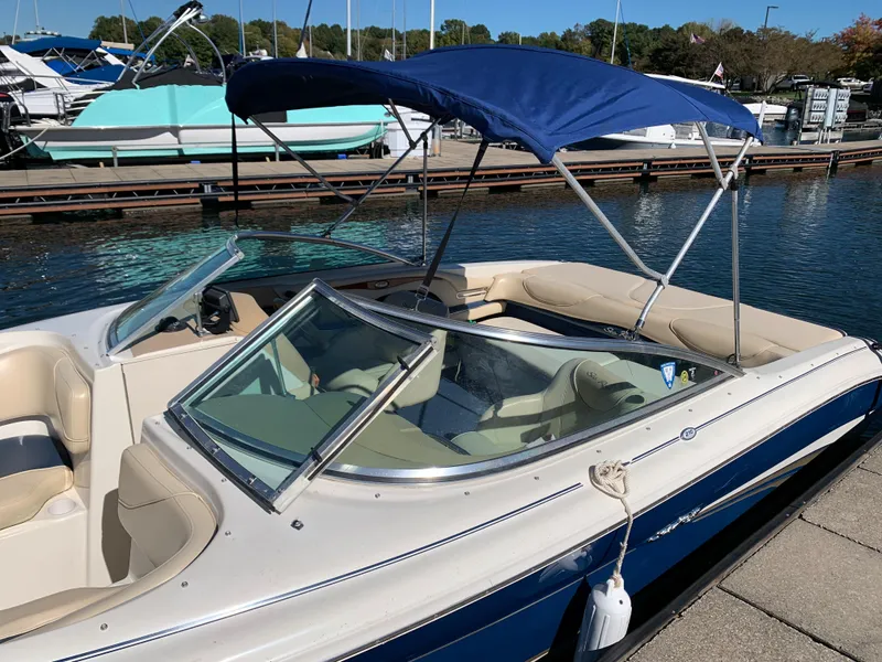 Slide: The Image of 2000 Sea Ray 210 Bow Rider boat docked with blue bimini top and beige interior. - 8