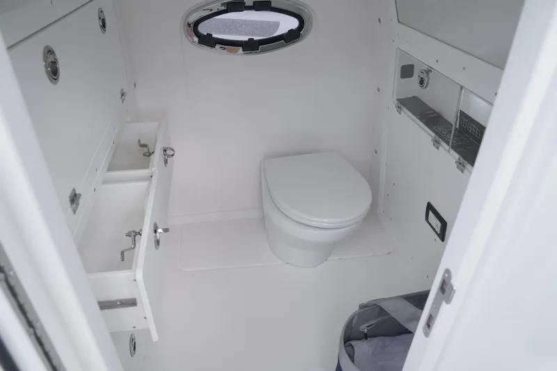 Slide: The Image of 2024 Caymas 34 CT boat bathroom with toilet, storage drawers, and porthole window. - 6