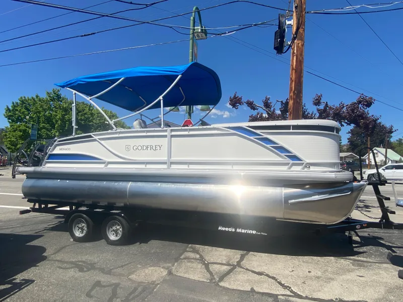 The Image of 2023 Godfrey Monaco 235 Rear Lounge pontoon boat with blue canopy on trailer. - 1