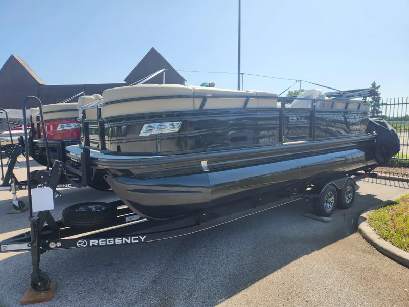 Slide: The Image of 2023 Regency 230 LE3 pontoon boat on a trailer in a dealership lot. - 0