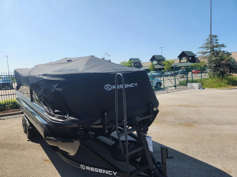 Slide: The Image of 2023 Regency 230 LE3 boat covered in black tarp, parked outdoors. - 3