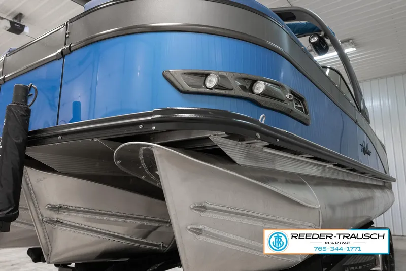 Slide: The Image of 2023 Avalon Waketoon pontoon boat in a showroom, featuring sleek blue and silver design. - 5