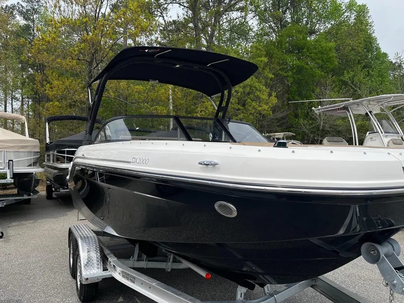 Slide: The Image of 2024 Bayliner DX2000 boat on trailer, black hull, white deck, bimini top, parked outdoors. - 3