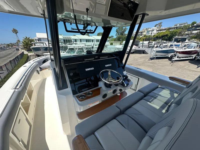 Slide: The Image of 2025 Boston Whaler 360 Outrage helm with modern controls and seating at a marina. - 11