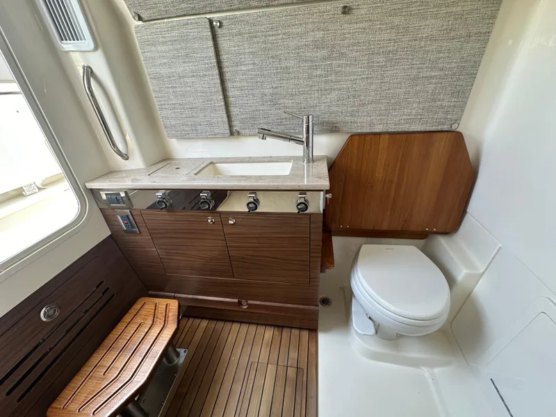 Slide: The Image of Interior of 2025 Boston Whaler 360 Outrage, featuring a compact bathroom with sink and toilet. - 24