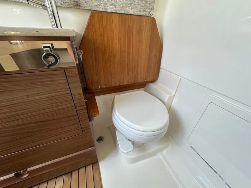 Slide: The Image of 2025 Boston Whaler 360 Outrage boat interior with wooden cabinetry and compact toilet. - 26