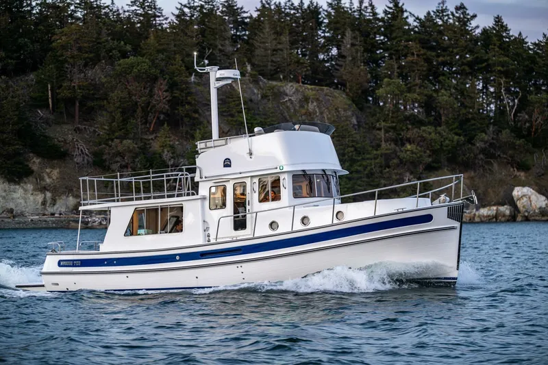 Slide: The Image of 2024 Nordic Tug 40 cruising on scenic waters near a forested shoreline. - 4