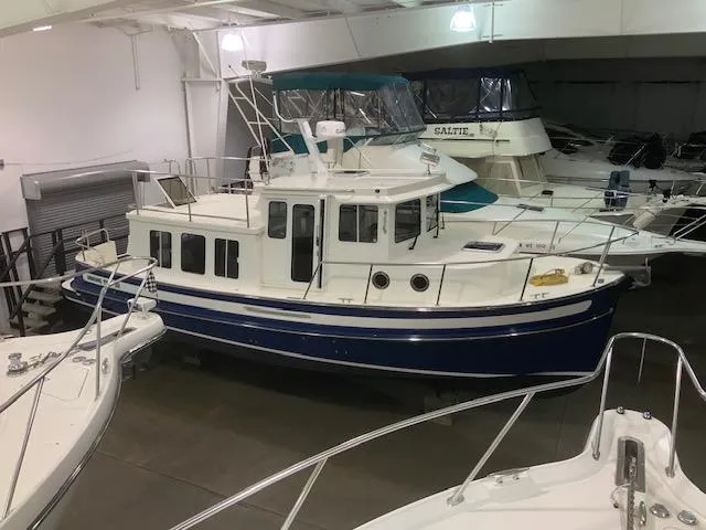 Slide: The Image of 2010 Nordic Tug 32 in a showroom, featuring a blue hull and white cabin. - 2