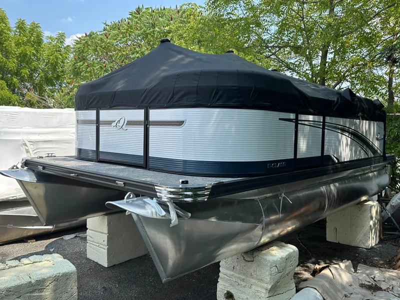 The Image of 2023 Qwest E 816 Lanai LT pontoon boat with black cover, parked on blocks. - 0
