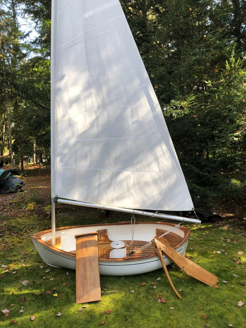 Slide: The Image of 1980 Tender Perrywinckle sailboat on grass, surrounded by trees, with wooden oars and white sail. - 4