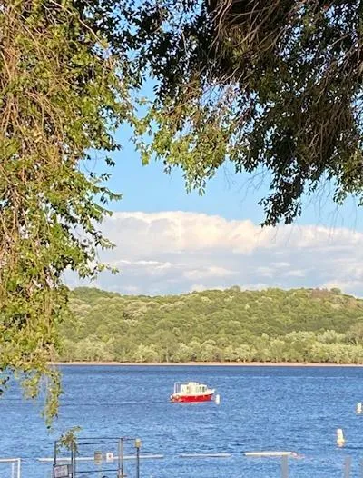 Slide: The Image of Red trawler on a serene lake, surrounded by lush greenery and a clear blue sky. - 19