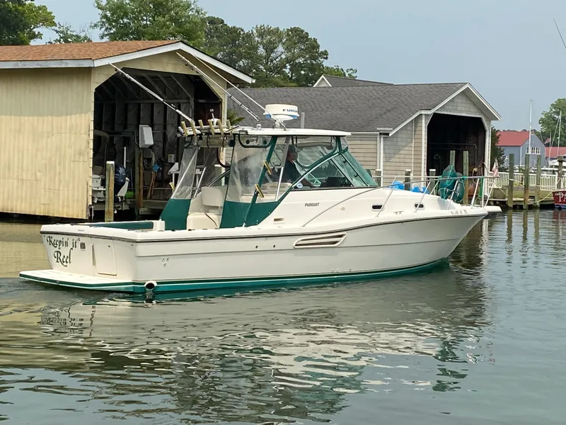 The Image of 2002 Pursuit 3000 Express boat docked near wooden boathouse on calm water. - 0