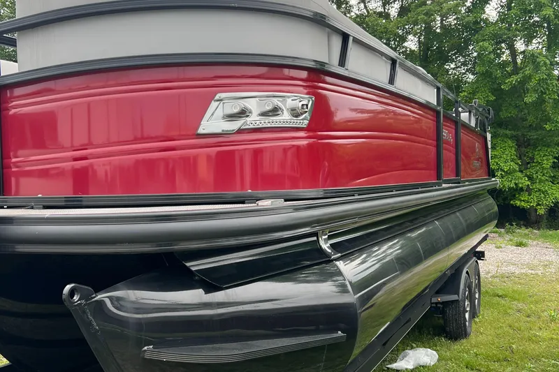 Slide: The Image of 2023 Regency 250 LE3 Sport pontoon boat, red and black, parked on grass. - 2