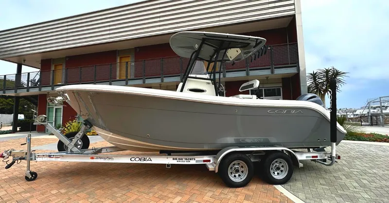 The Image of 2023 Cobia Center Console 220 boat on a trailer in front of a modern building. - 1
