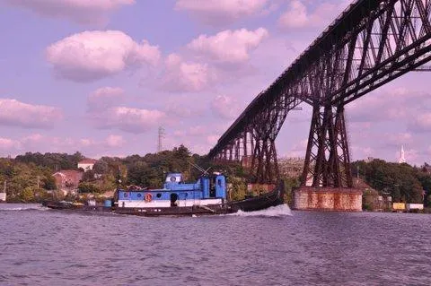 Slide: The Image of Blue Johnson Brother Tug 64 (1903) tugboat under a large bridge on a river. - 1
