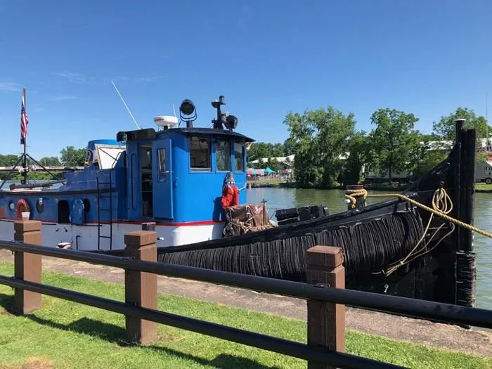 Slide: The Image of 1903 Johnson Brother Tug 64 docked by a riverside park on a sunny day. - 2