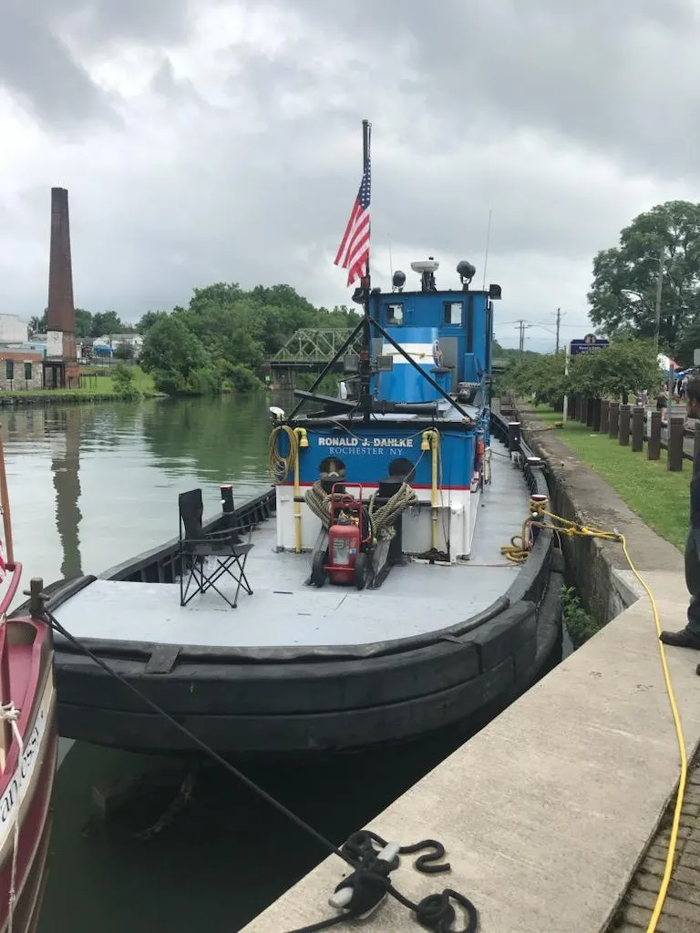 Slide: The Image of Historic 1903 Johnson Brother Tug 64 docked by a canal with an American flag. - 3