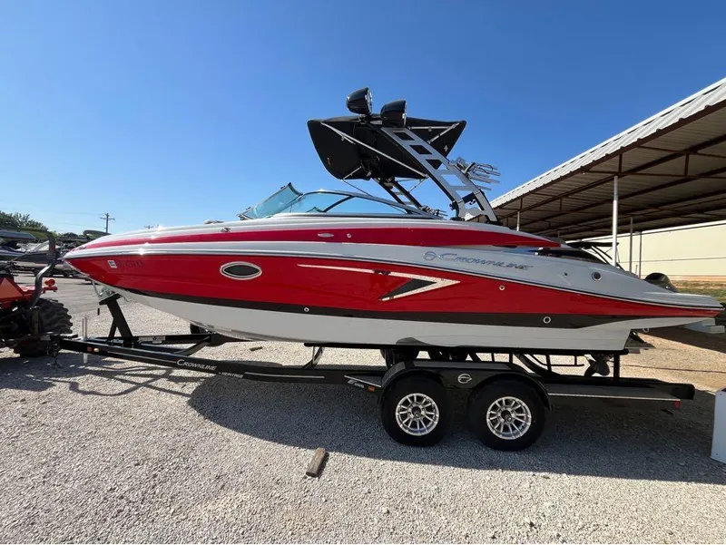 Slide: The Image of 2023 Crownline E255 Surf boat on trailer, red and white design, parked outdoors. - 6
