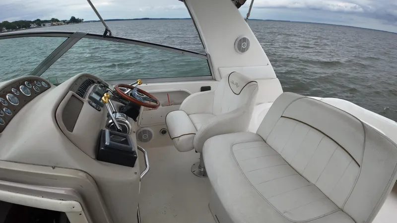 Slide: The Image of 1999 Sea Ray 310 Sundancer boat interior with steering wheel and seating, on open water. - 10