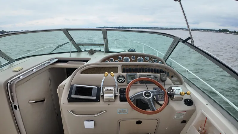 Slide: The Image of 1999 Sea Ray 310 Sundancer helm with steering wheel and control panel on open water. - 16