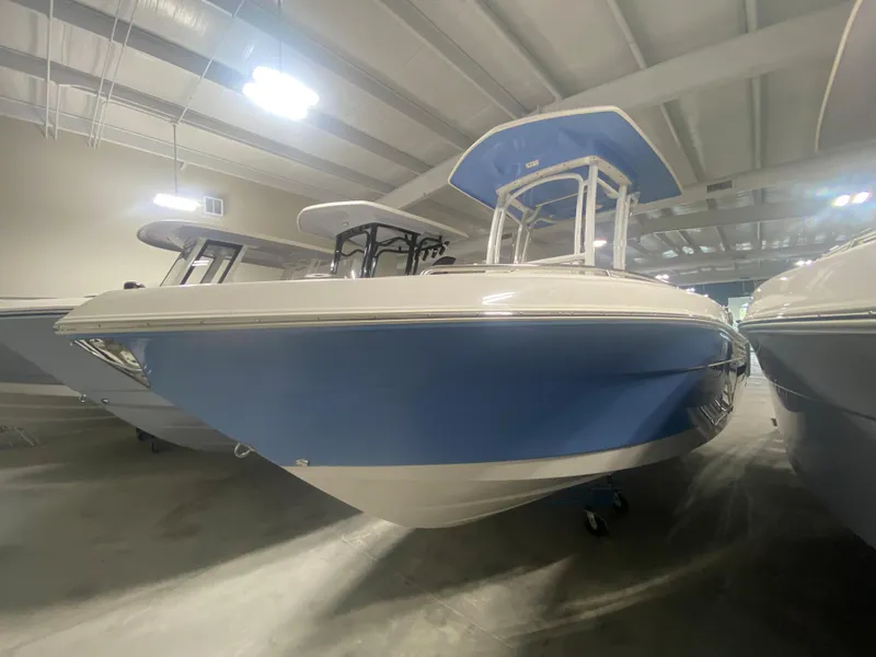 Slide: The Image of 2024 Robalo R222 boat in showroom, blue and white hull, under bright lights. - 0