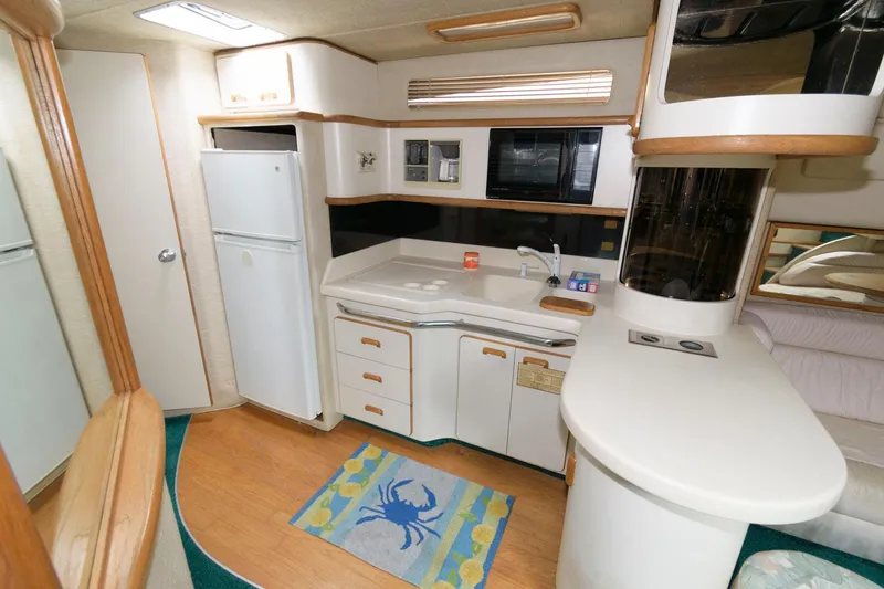 Slide: The Image of 1993 Sea Ray 500 Sundancer yacht kitchen with white cabinets, fridge, and blue crab rug. - 13