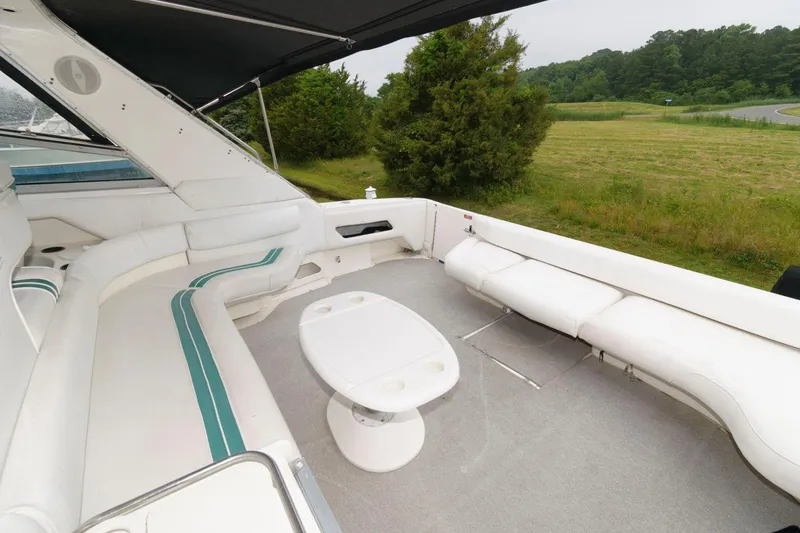 Slide: The Image of 1993 Sea Ray 500 Sundancer boat deck with white seating and table, surrounded by greenery. - 3