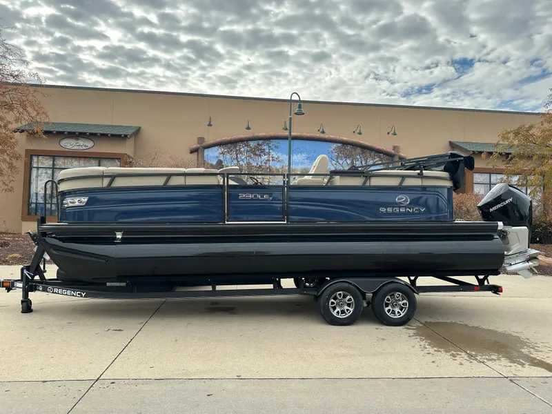 Slide: The Image of 2023 Regency 230 LE3 pontoon boat on a trailer, parked outdoors. - 0