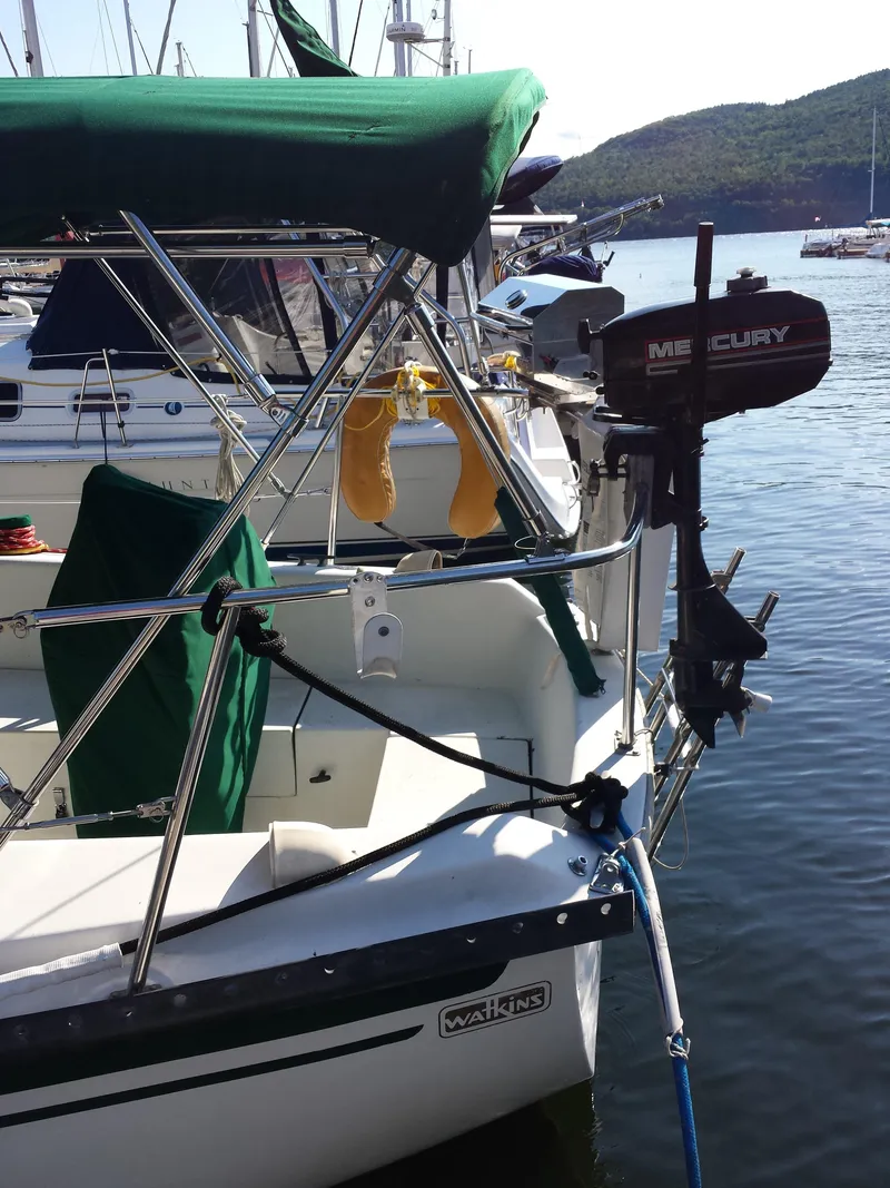 Slide: The Image of 1983 Watkins 32 sailboat docked with Mercury outboard motor, green canopy, and scenic background. - 2