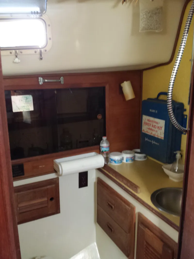 Slide: The Image of Compact kitchen area in a 1983 Watkins 32 sailboat with wooden cabinets and a first aid kit. - 27