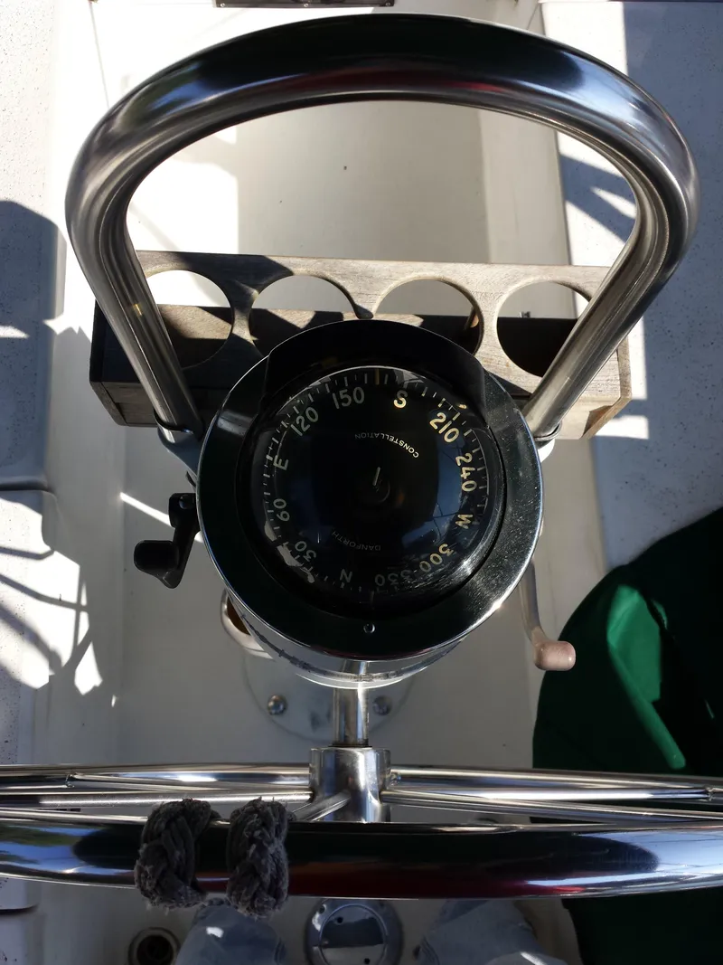 Slide: The Image of Compass on 1983 Watkins 32 sailboat helm, featuring stainless steel wheel and cup holders. - 5