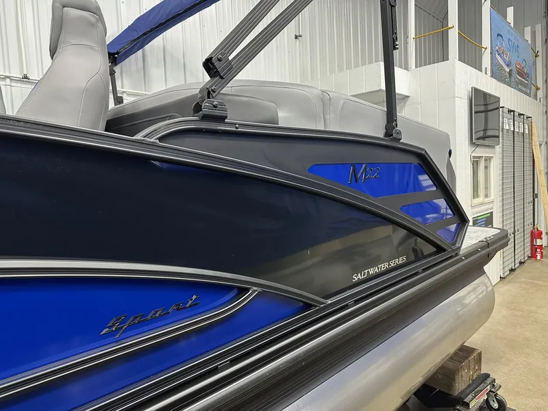 Slide: The Image of 2025 Bennington 22 MFB Tritoon, blue and black, in showroom, featuring quad bench seating. - 24