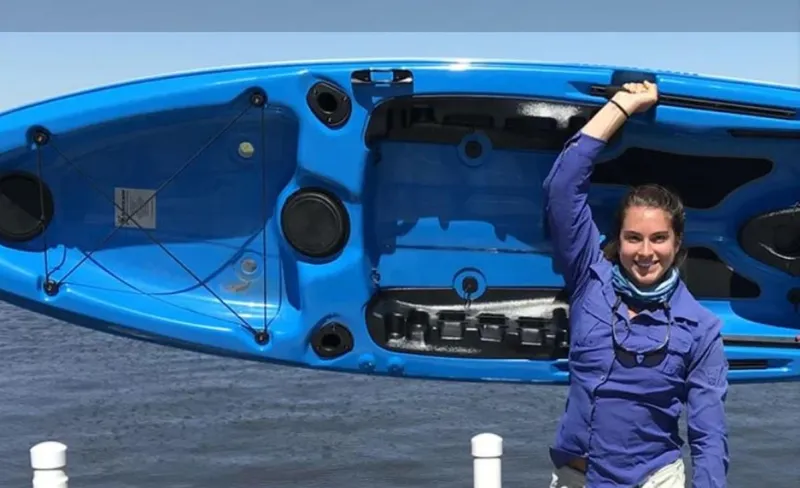 Slide: The Image of Person holding a blue 2023 Hurricane Kayaks Sweetwater 126 kayak by the water. - 2