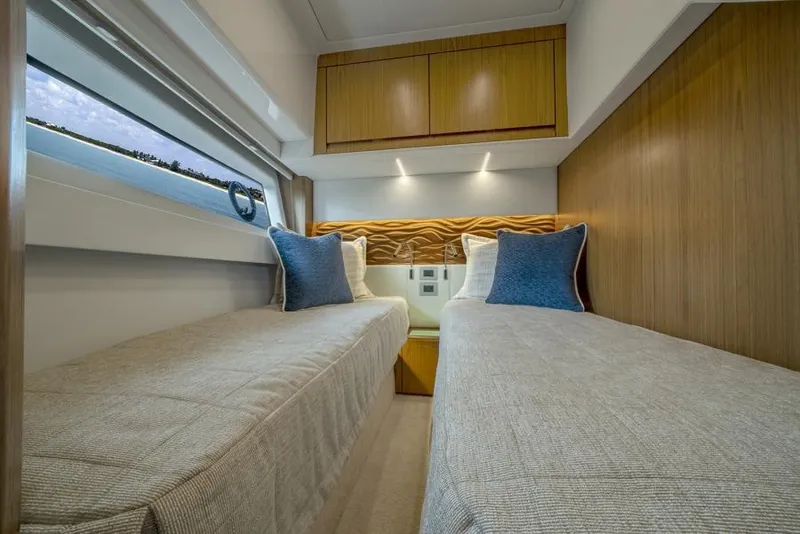 Slide: The Image of 2025 Tiara Yachts EX60 twin bed cabin with modern wood finishes and blue accent pillows. - 35