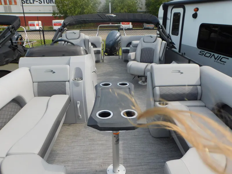 Slide: The Image of 2023 Bennington 23LFB pontoon boat interior with gray seating and table, parked near RV. - 9
