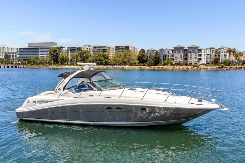 The Image of 2005 Sea Ray 390 Sundancer yacht cruising on a sunny day near waterfront buildings. - 0