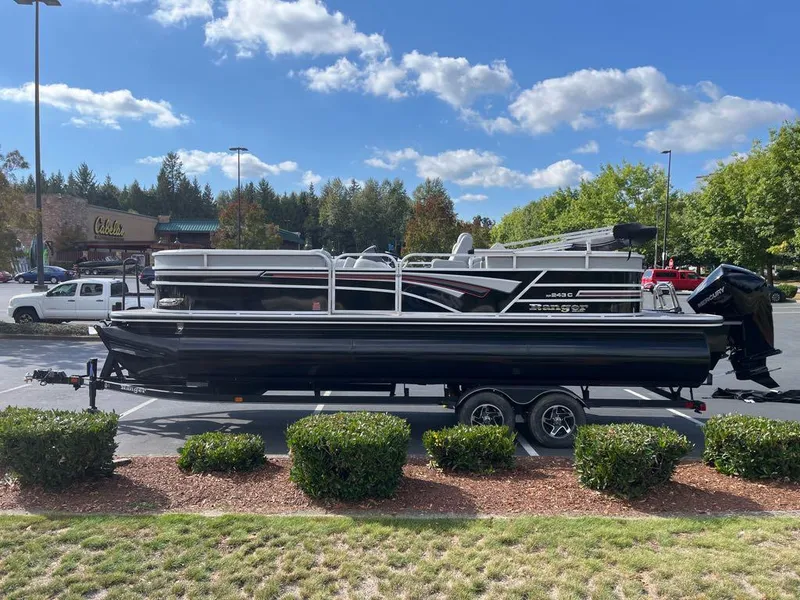 The Image of 2023 Ranger Reata 243C pontoon boat on a trailer in a parking lot. - 0